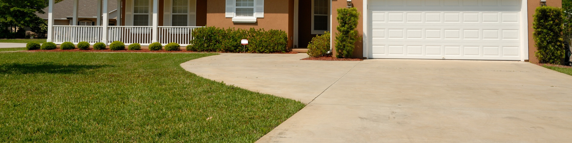 A tan-colored single-story suburban house with a white garage door and a curved concrete driveway leading to the entrance.