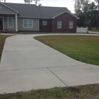 A newly paved concrete driveway leading toward a modern house with tan siding and a red brick section.