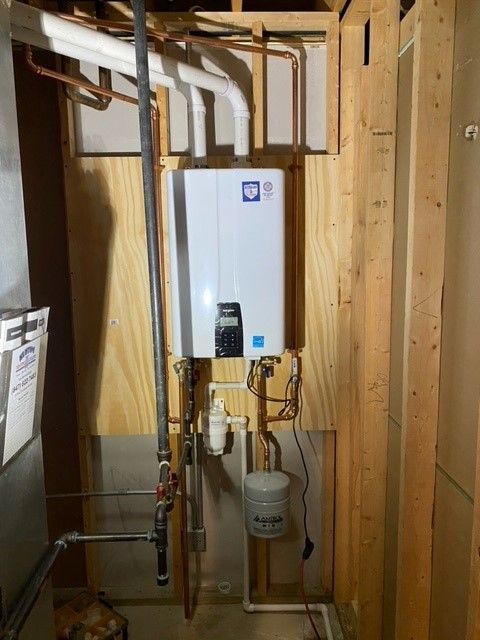 Tankless water heater installed in a wooden frame with associated pipes and components.