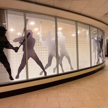 Hallway with curved windows displaying baseball batter silhouettes in shades of purple and grey.