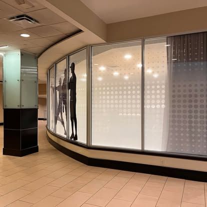 A curved storefront window displaying mannequins and a patterned frosted design inside a mall hallway.
