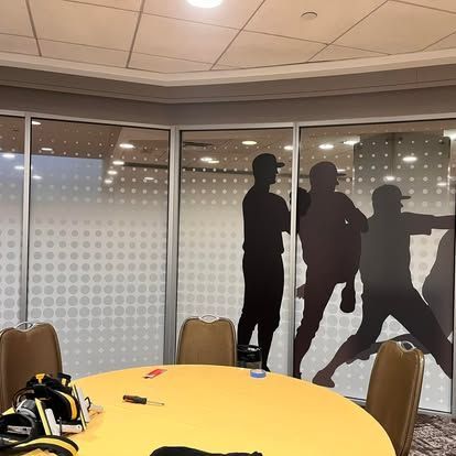 A conference room featuring a yellow table surrounded by chairs. Frosted glass panels depict baseball player silhouettes.