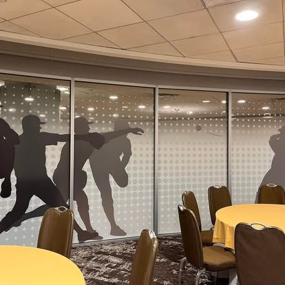A restaurant dining area with baseball player silhouettes on the windows and tables with yellow tablecloths.