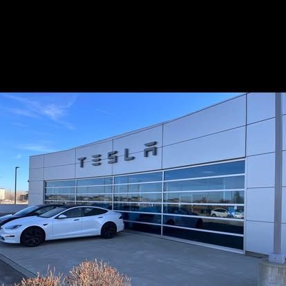 Tesla dealership exterior with white and gray cars parked outside the building with large glass windows. The 