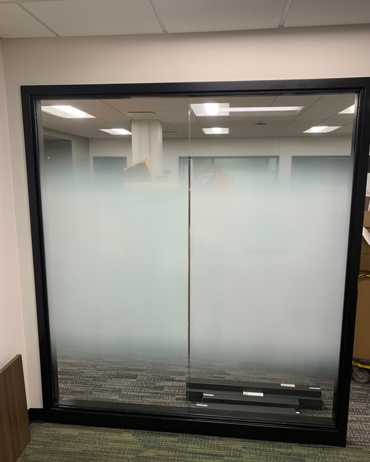 Glass office wall with a frosted middle section and a black frame, reflecting the interior.