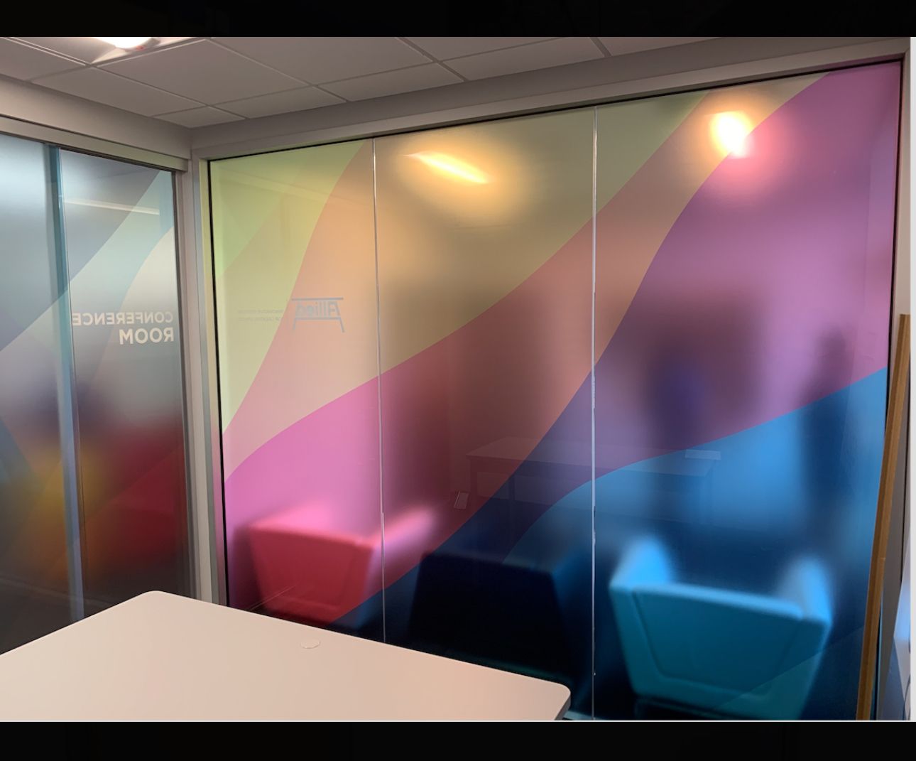 A small, brightly colored office space with frosted glass walls and colorful seating.