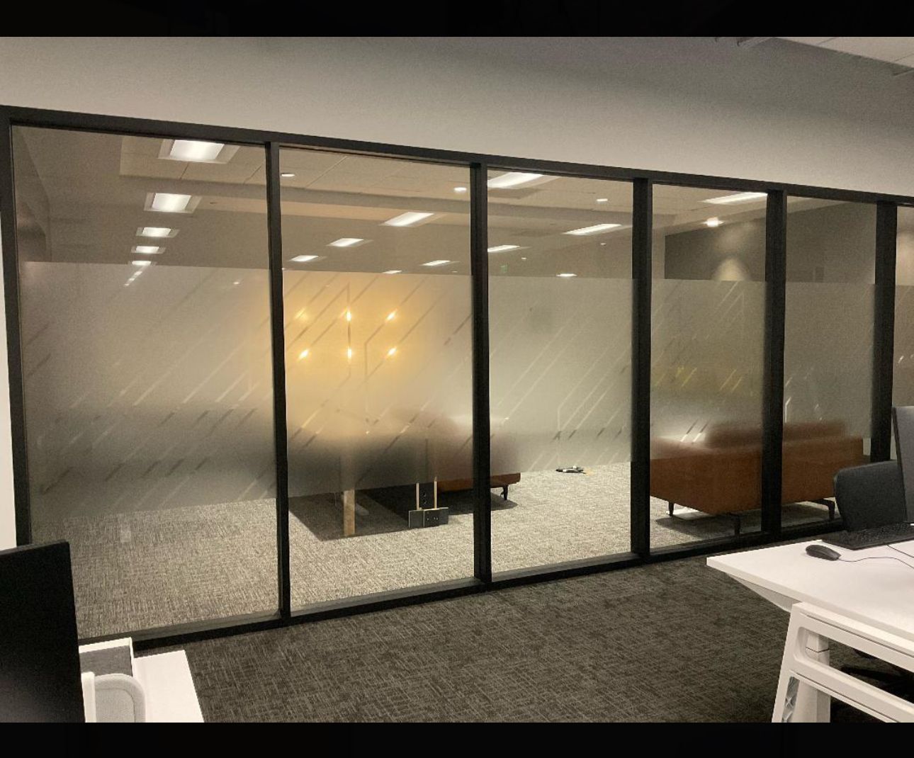 Office interior with glass-walled room. Frosted glass provides privacy. Includes a lounge area with brown sofa and desk.