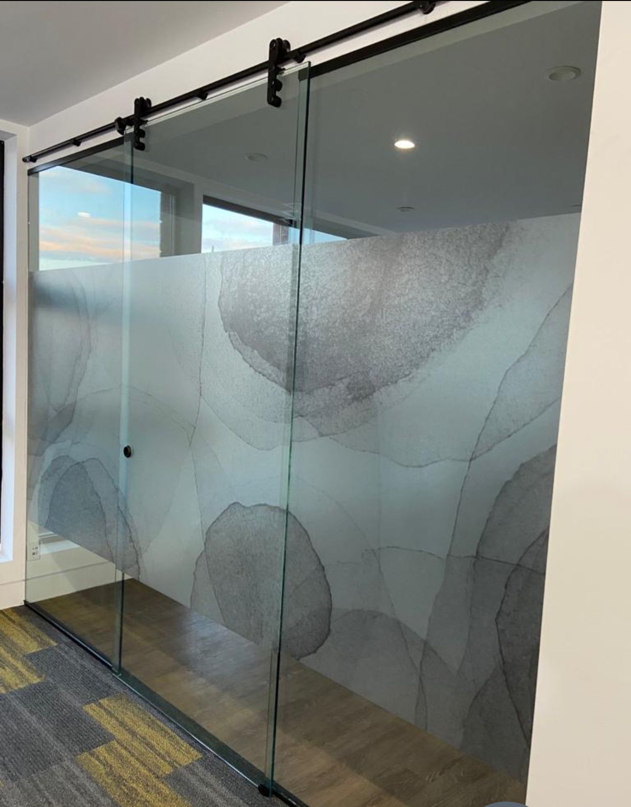 Glass sliding door with abstract gray pattern on a frosted section. The door has a black track and hardware, with a glimpse of a colorful carpet.