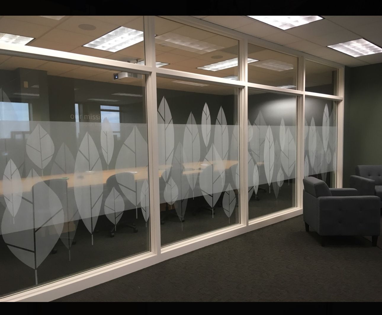 Conference room with frosted glass windows decorated with leaf patterns; gray furniture and carpet.