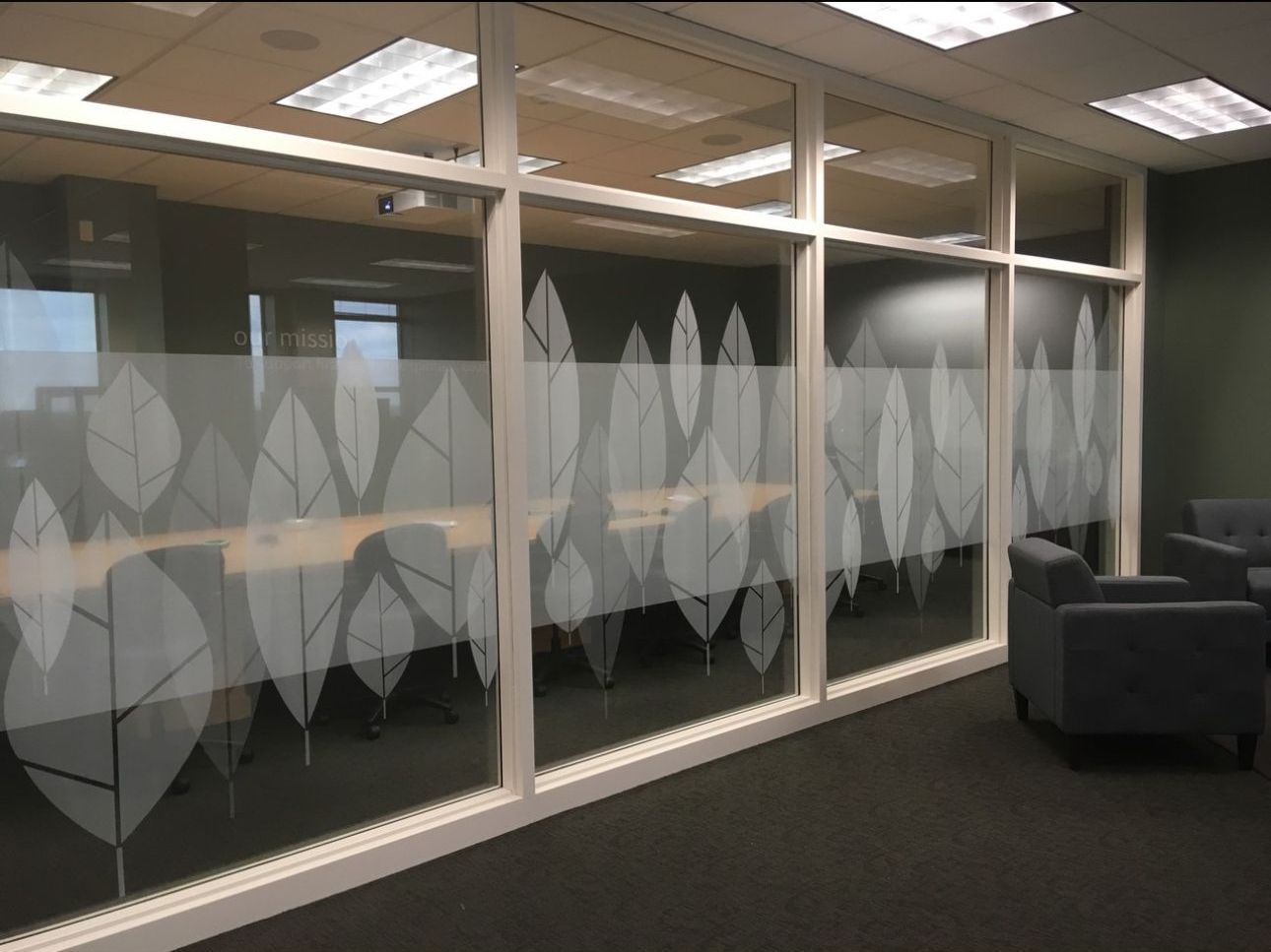 A modern office space with frosted glass panels adorned with leaf designs. Chairs sit in front of the conference room, offering seating.