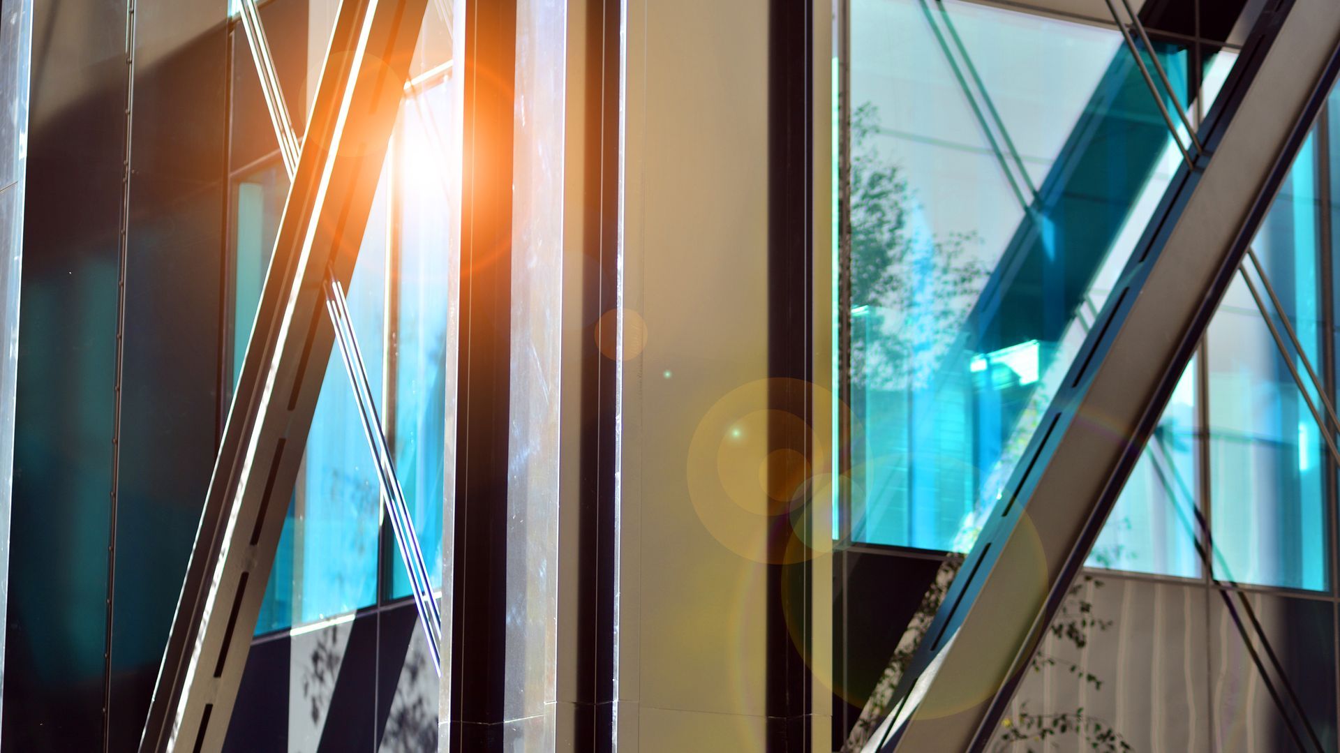 Close-up of a modern building's architectural details: steel beams, reflective glass windows, and sunlight.