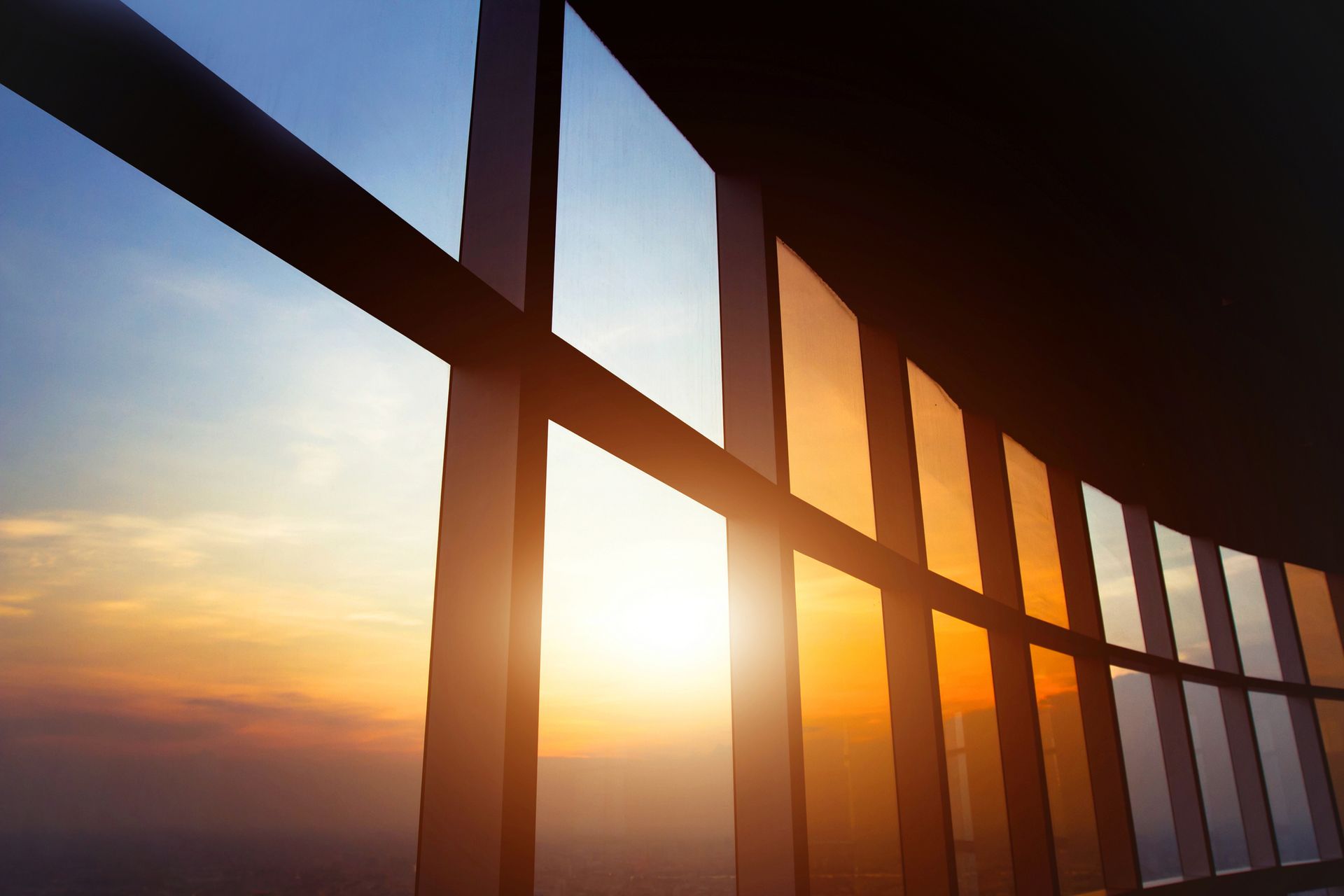 Sunset through curved, tinted windows of a tall building, highlighting the orange and blue sky.