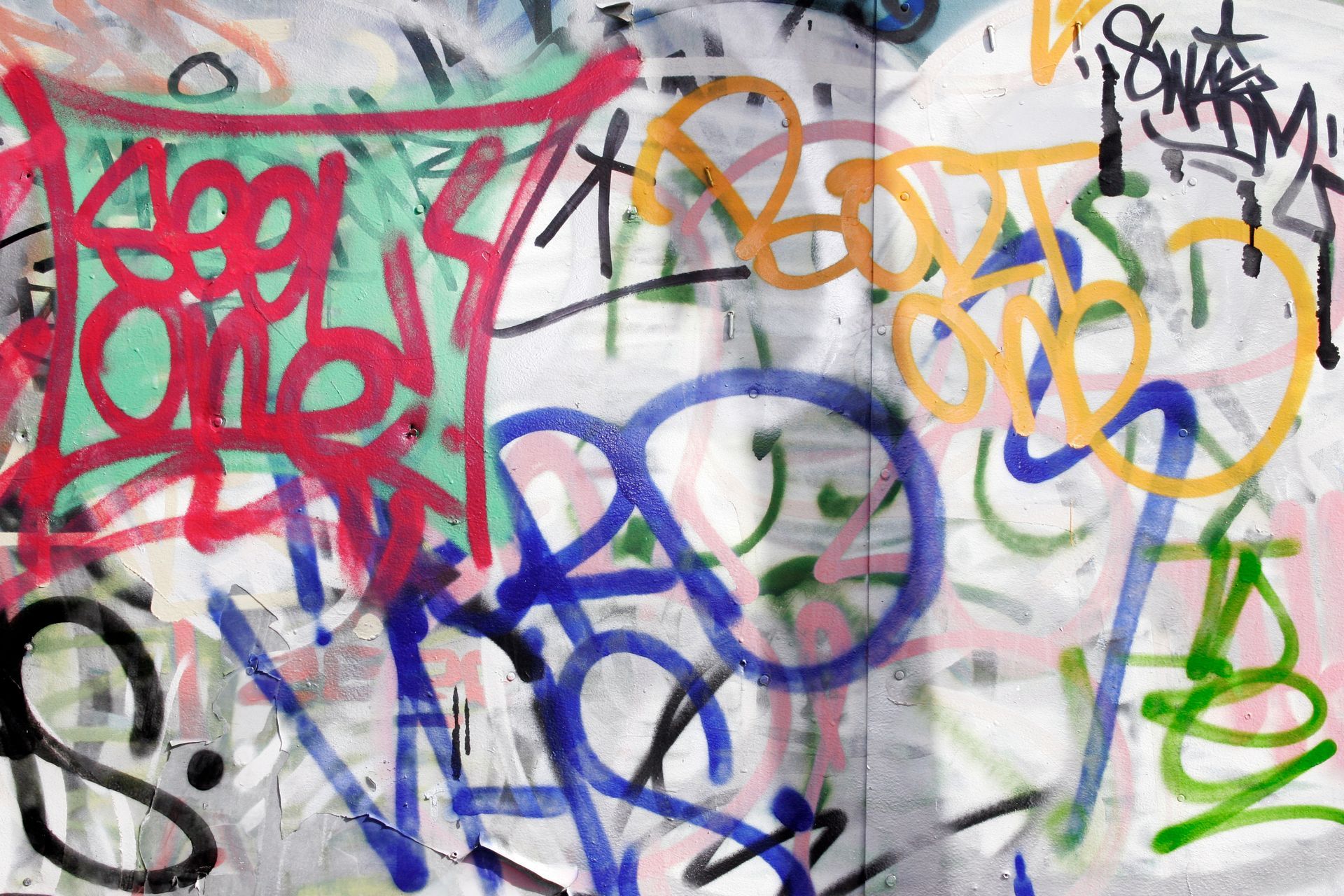 Graffiti on a wall featuring various colorful tags and spray-painted words.