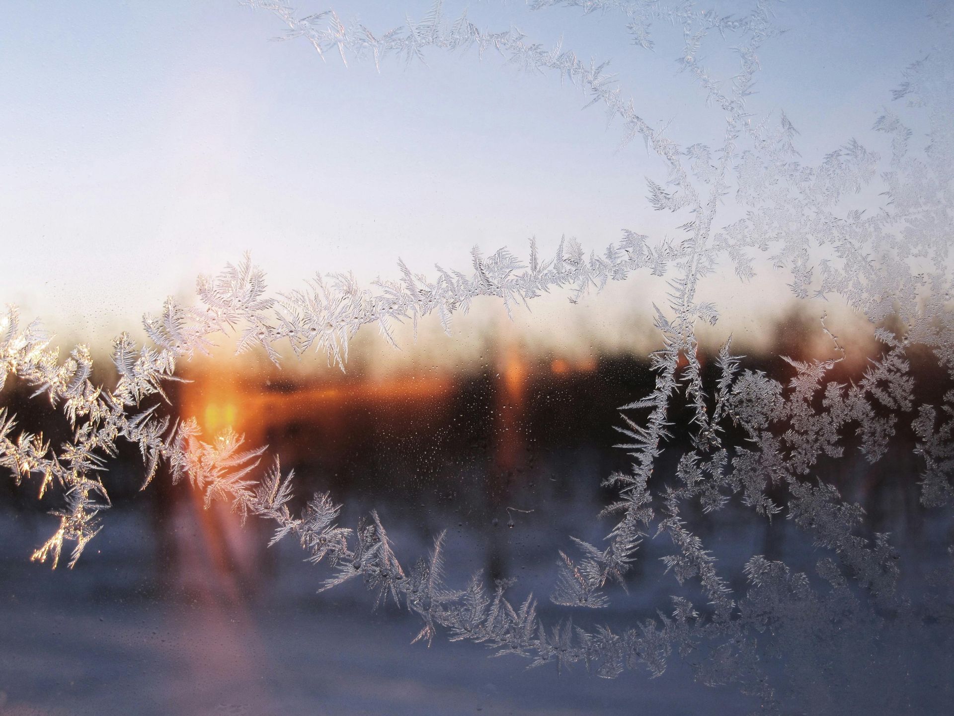 Frost patterns on a windowpane, with a blurred sunset visible through it.