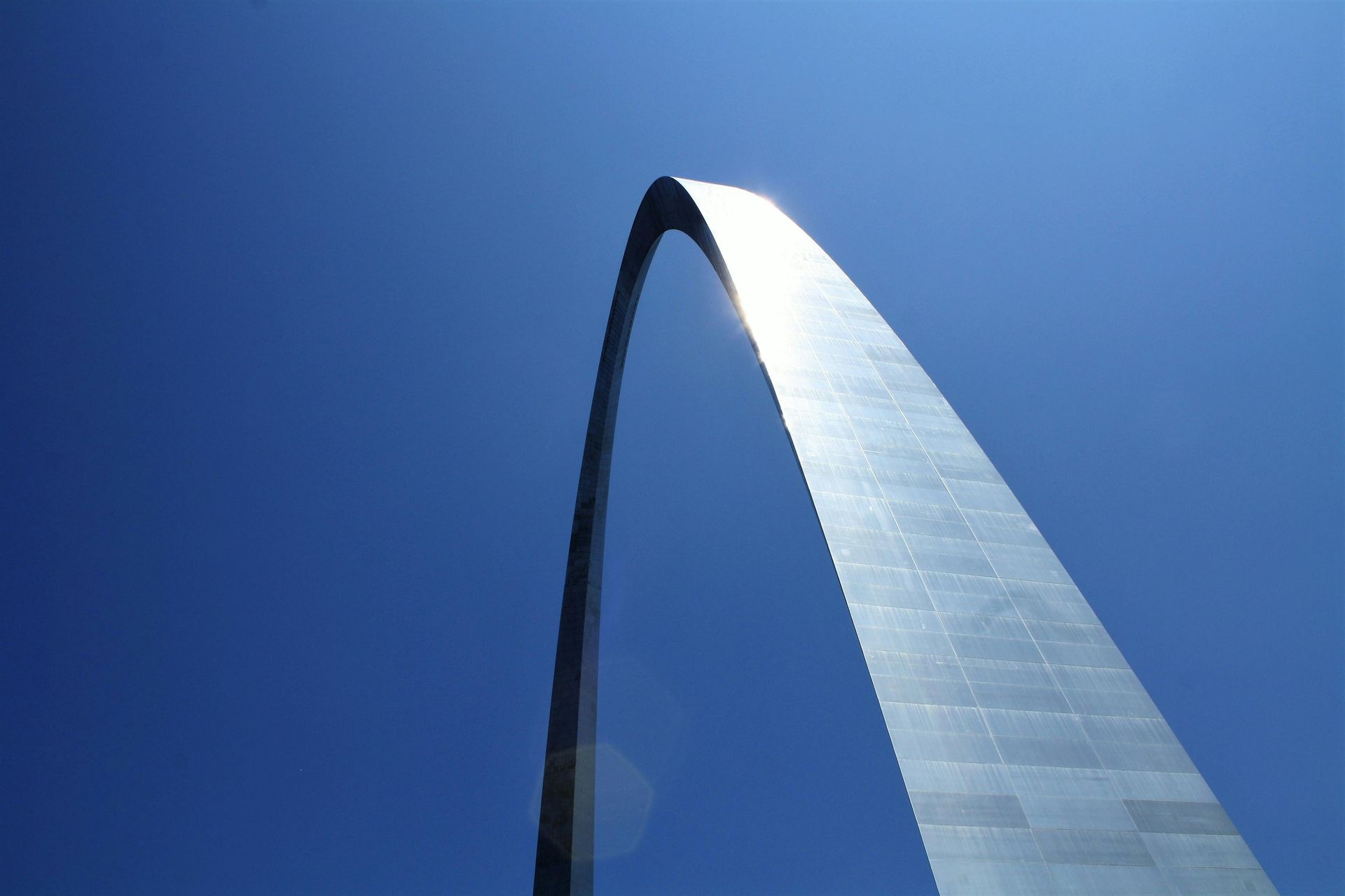 The Gateway Arch in St. Louis, Missouri, rises against a bright blue sky. The stainless steel monument curves upward.