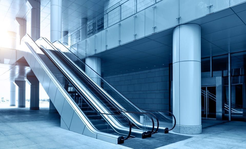 Escalators ascending inside a modern building. Blue-toned lighting and architecture with large pillars.