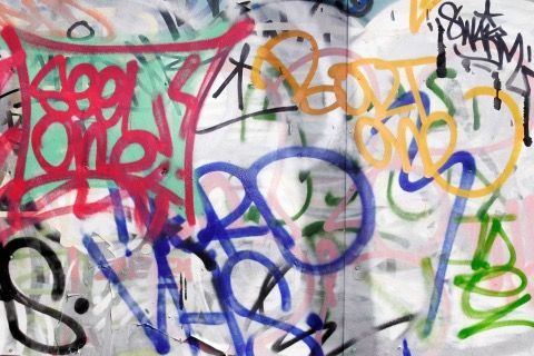 Graffiti on a wall featuring various colorful tags and spray-painted words.