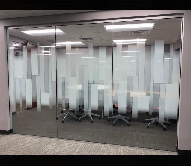 Meeting room with frosted glass walls, chairs, and a table visible through the glass. The room is brightly lit.