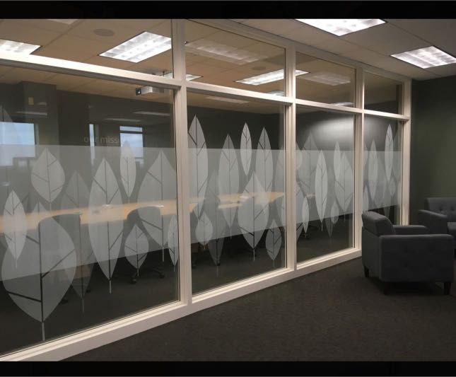 Glass office wall with white leaf pattern, revealing a conference room and waiting area.