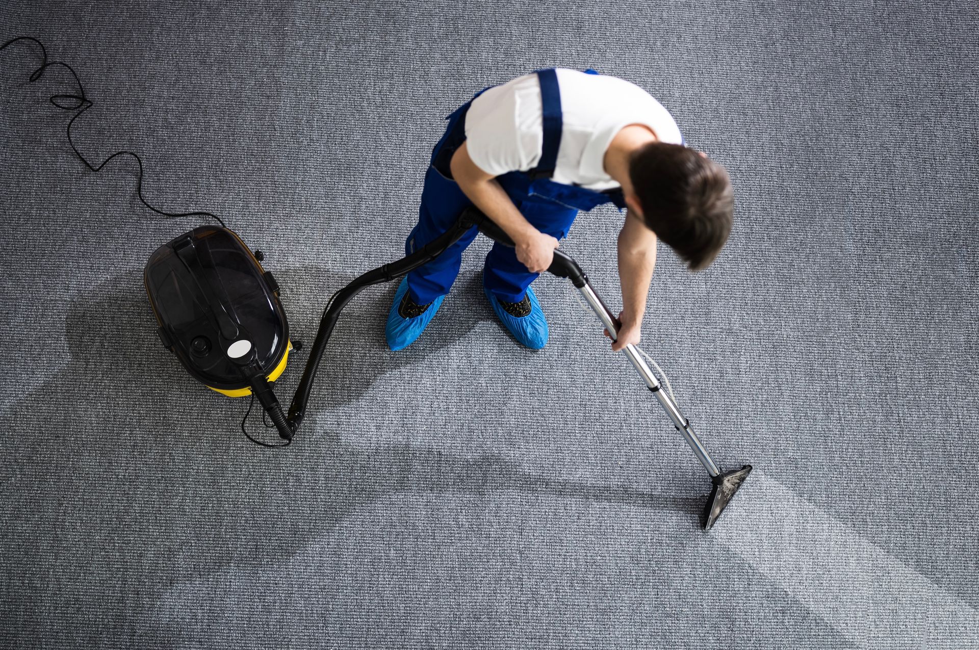 A man is cleaning a carpet with a vacuum cleaner.