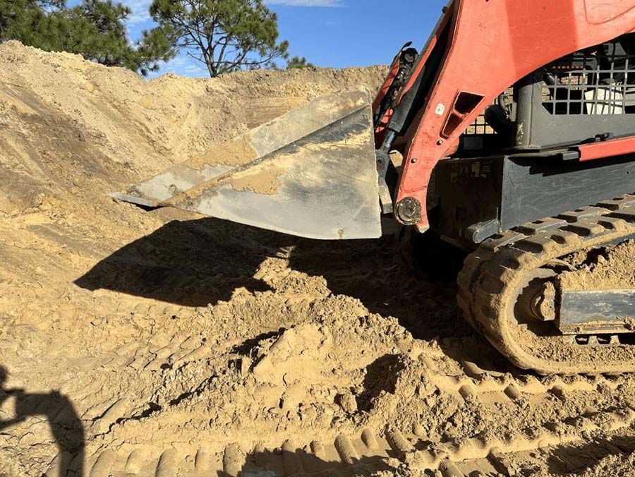 A red skid steer with a bucket, excavating dirt in a sunny, outdoor setting.