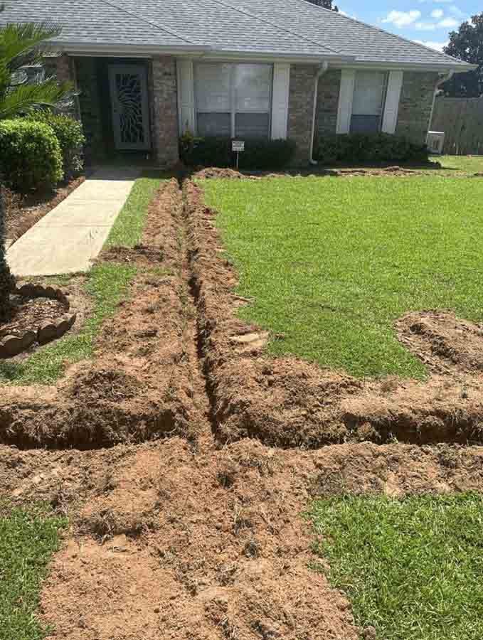 A trench dug in a front lawn leads to a house; dirt piles on grass.