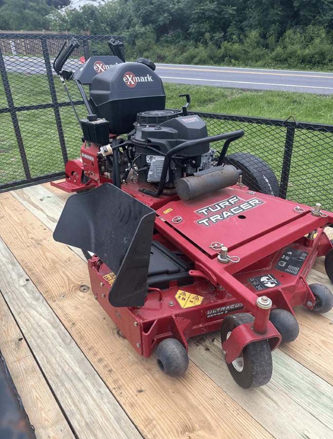 Red lawn mower on a wooden trailer, ready for transport.  Black engine and handles.