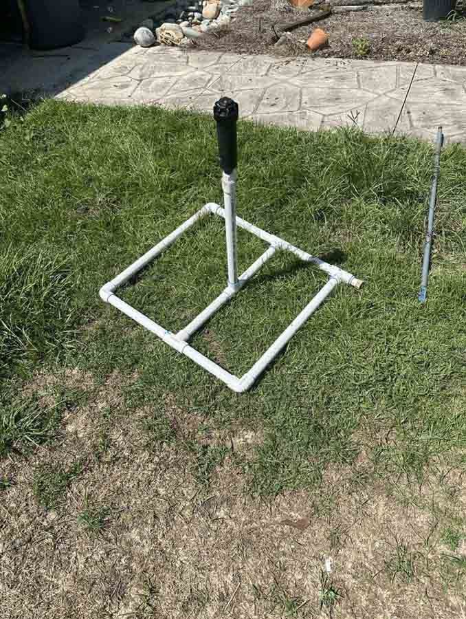 White PVC tee stand on green grass, ready for baseball practice outdoors.