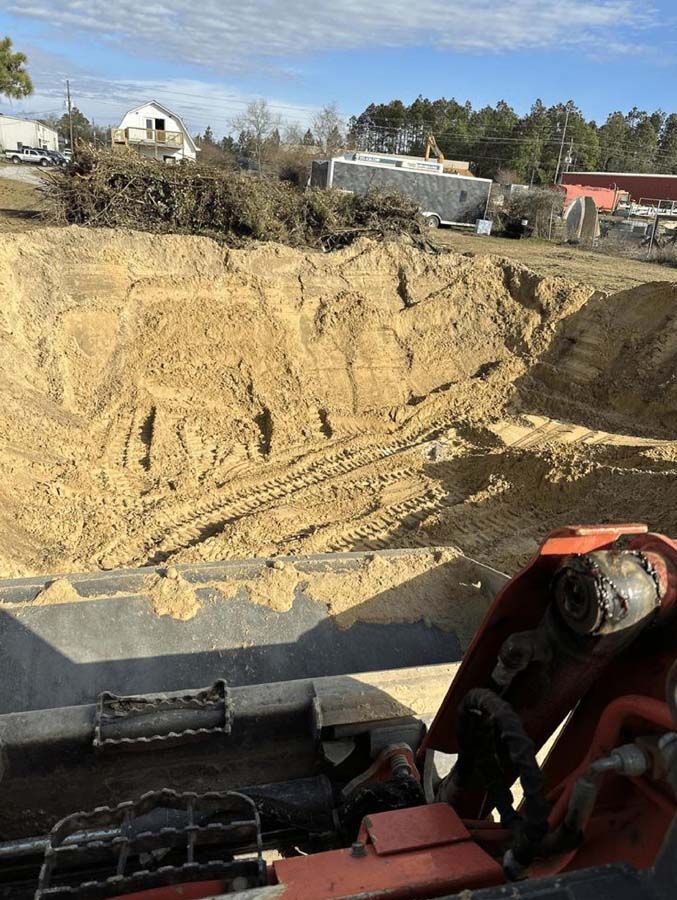 A backhoe bucket filled with dirt in front of a large excavation pit on a sunny day.