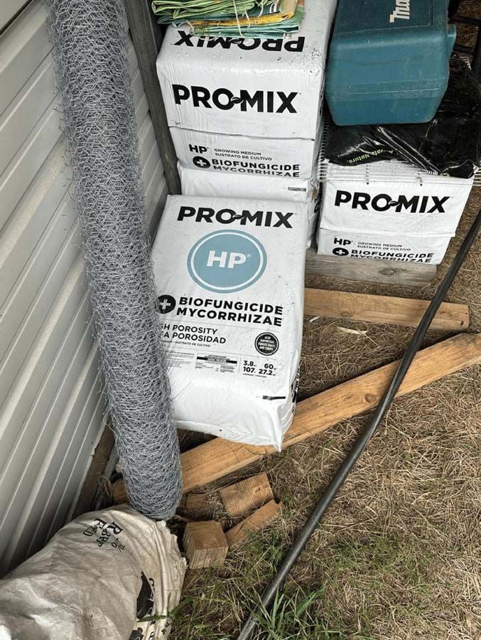 A roll of wire, bags of PRO-MIX HP, and tools are stored against a white wall.