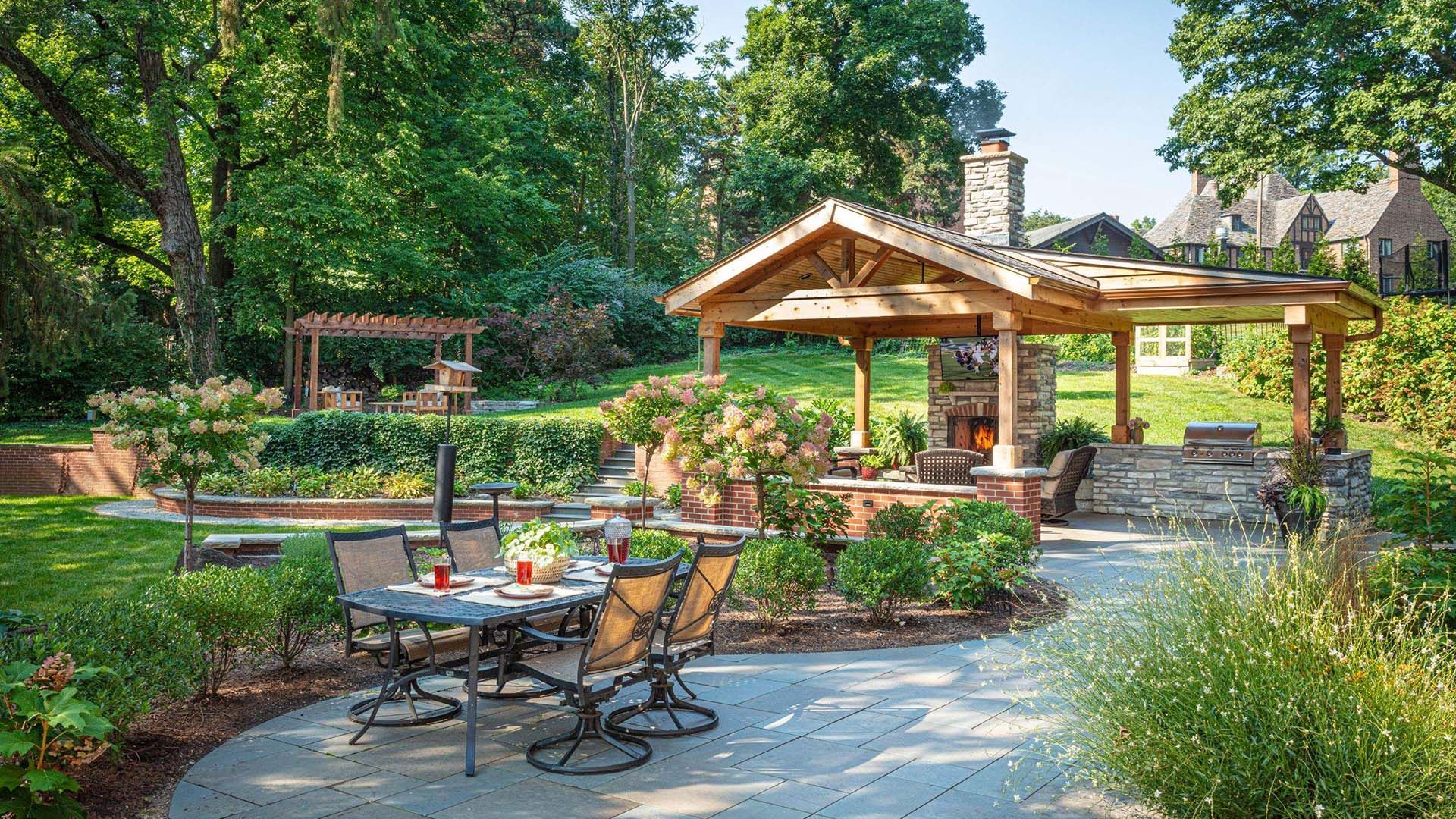 Patio with outdoor seating, fireplace, and a gazebo in a lush, green backyard.