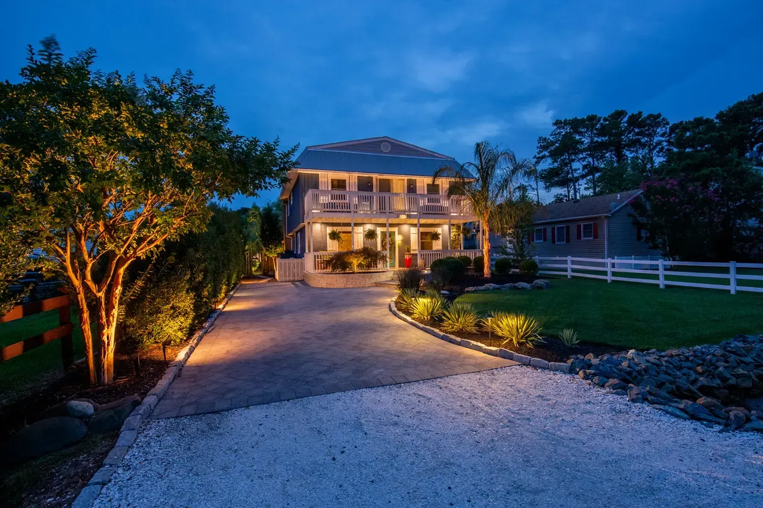 Two-story home with lit driveway and landscaping at dusk.