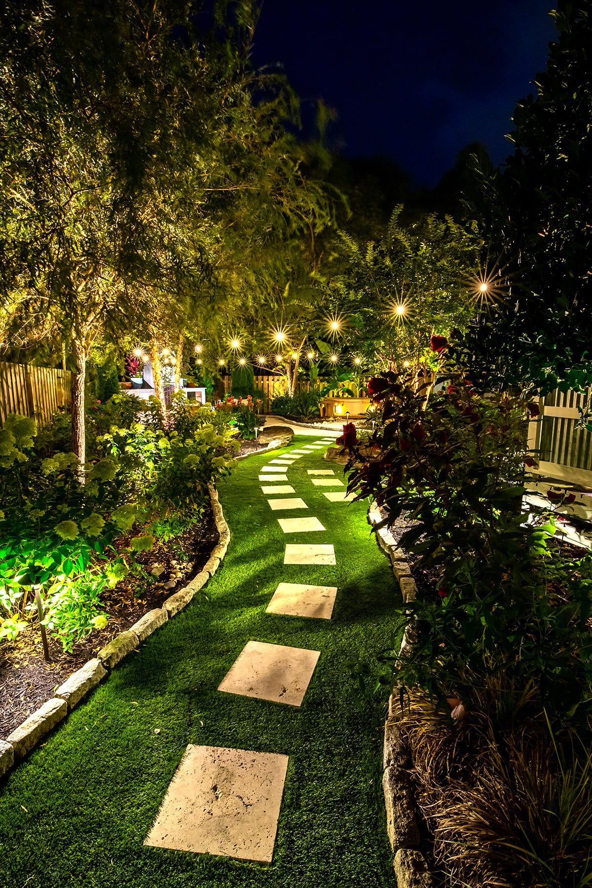 Stone path through a garden at night, illuminated by lights.
