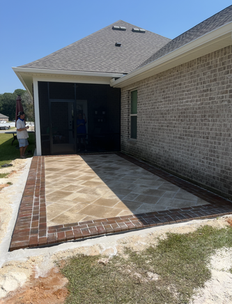 Patio with brick border and stone pavers, attached to a brick house, partially screened.