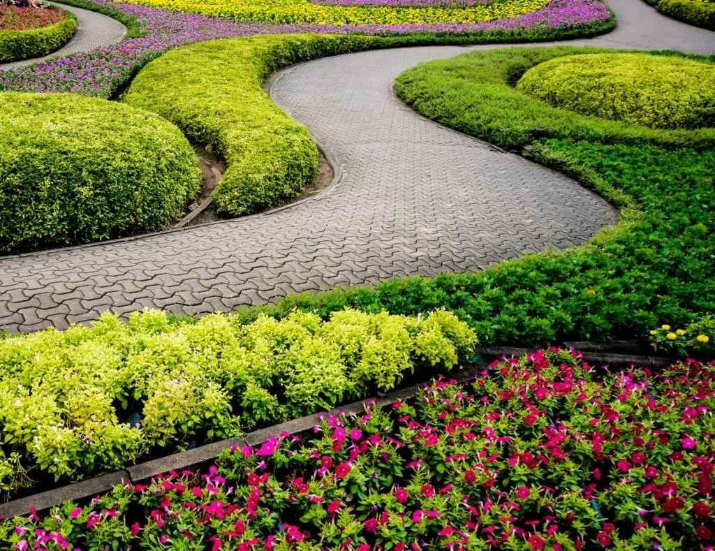 Curving gray stone path through a vibrant garden with green and purple flowers.