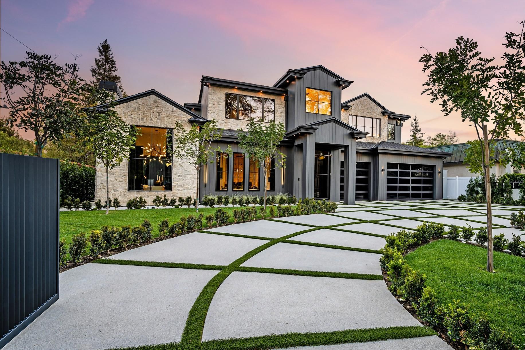 Luxurious two-story home with light brick, dark trim, and a patterned driveway at sunset.