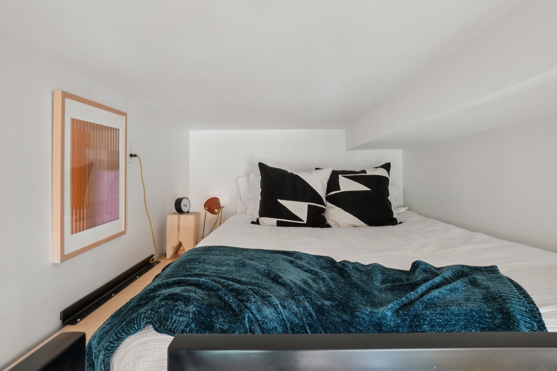 A bed with a blue blanket and two pillows with black and white patterns.