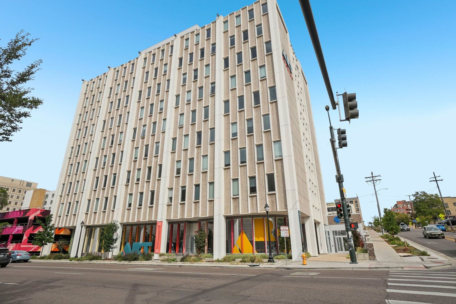 Multi-story building with vertical panels, windows, and colorful ground-level storefronts at a street intersection.