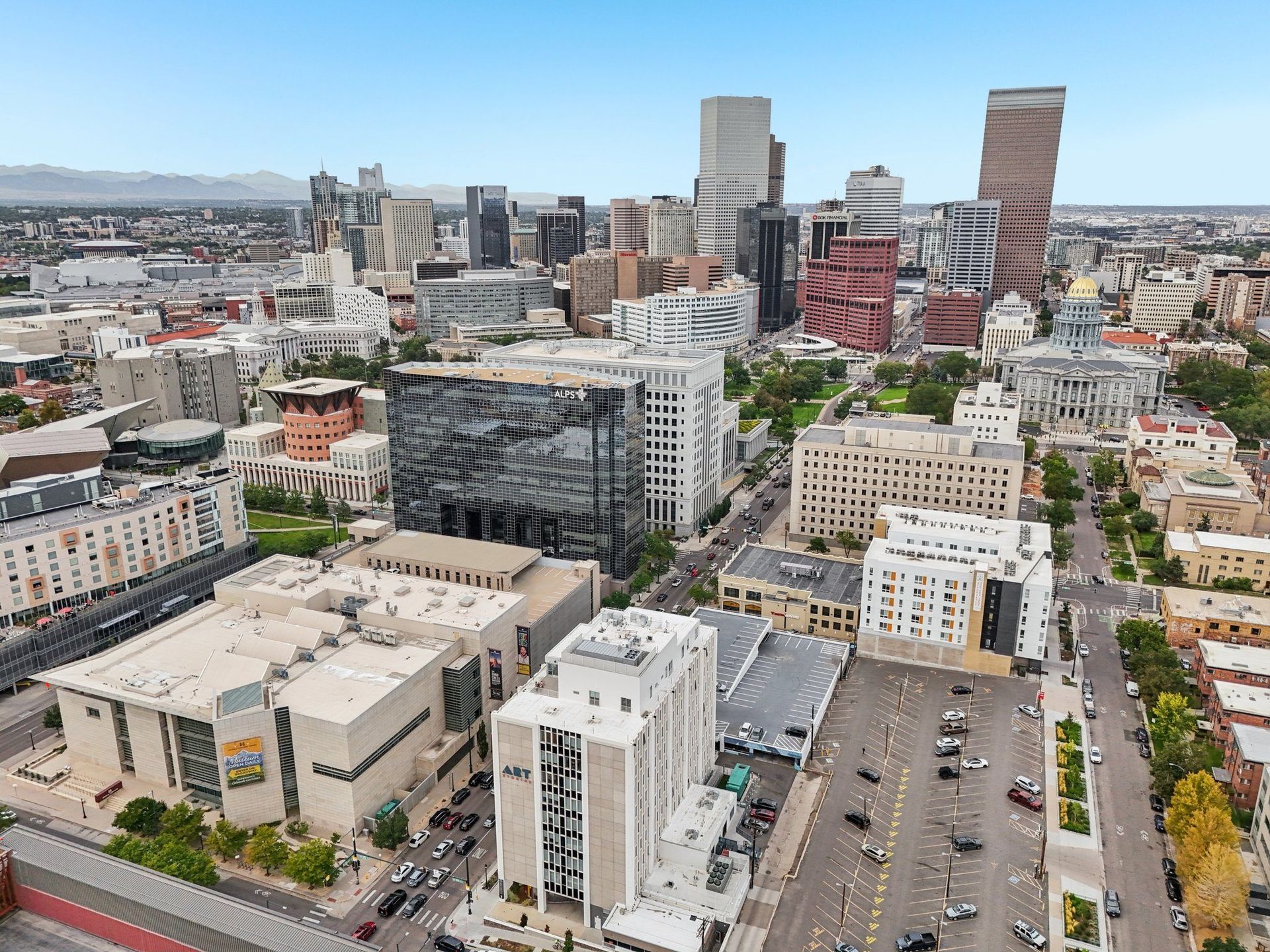 A cityscape with a mix of modern and older buildings, a clear sky, and a distant mountain range.