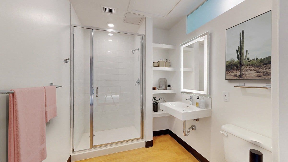 Modern bathroom with white walls, glass shower, and desert landscape art.