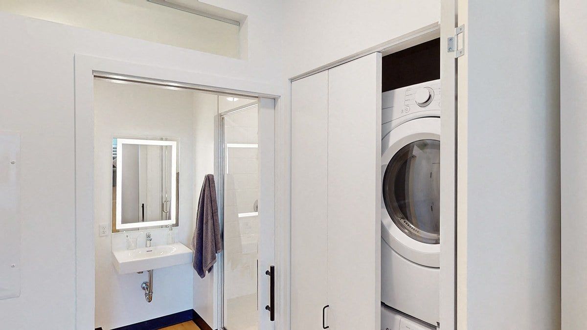Bathroom with washer/dryer in a closet, white walls, and a hanging towel.