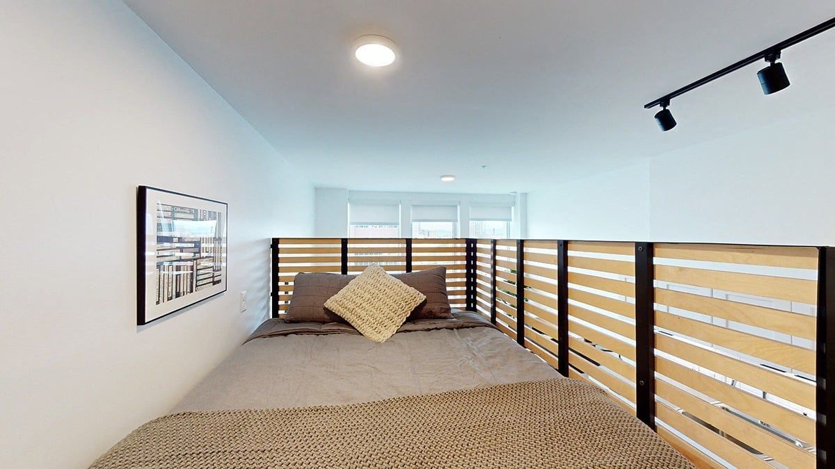 Bedroom with bed framed by wooden panels, art on wall, and track lighting.