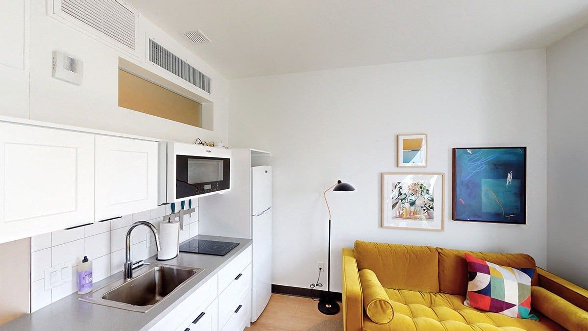 Small, modern studio apartment with kitchen, sofa, and artwork on the wall. White and gold color scheme.