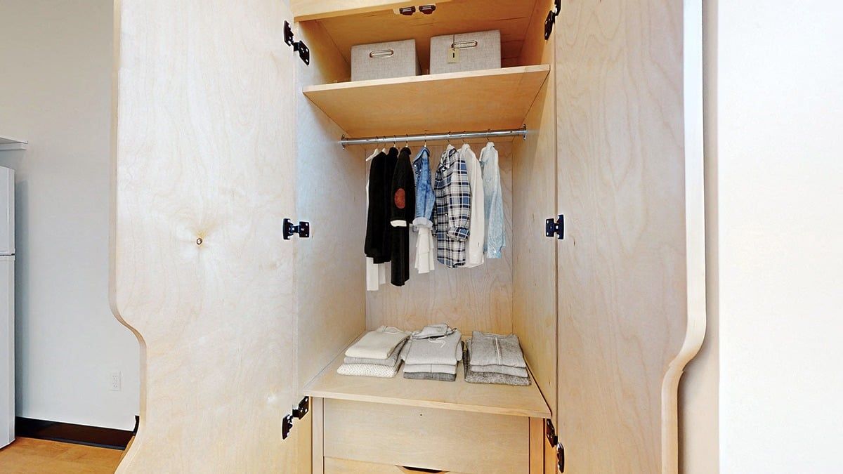 Wooden closet with clothes hanging and folded, two storage boxes on top shelf.