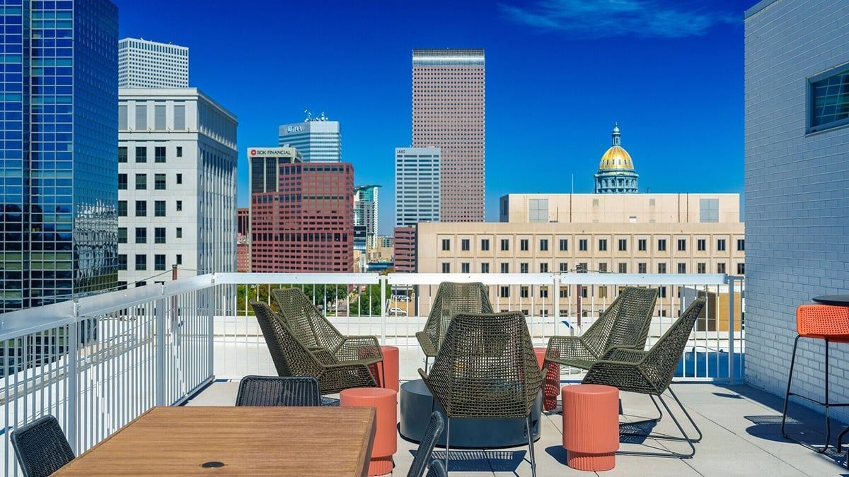Rooftop patio with chairs, tables, and city skyline view, featuring blue sky, buildings, and a gold dome.