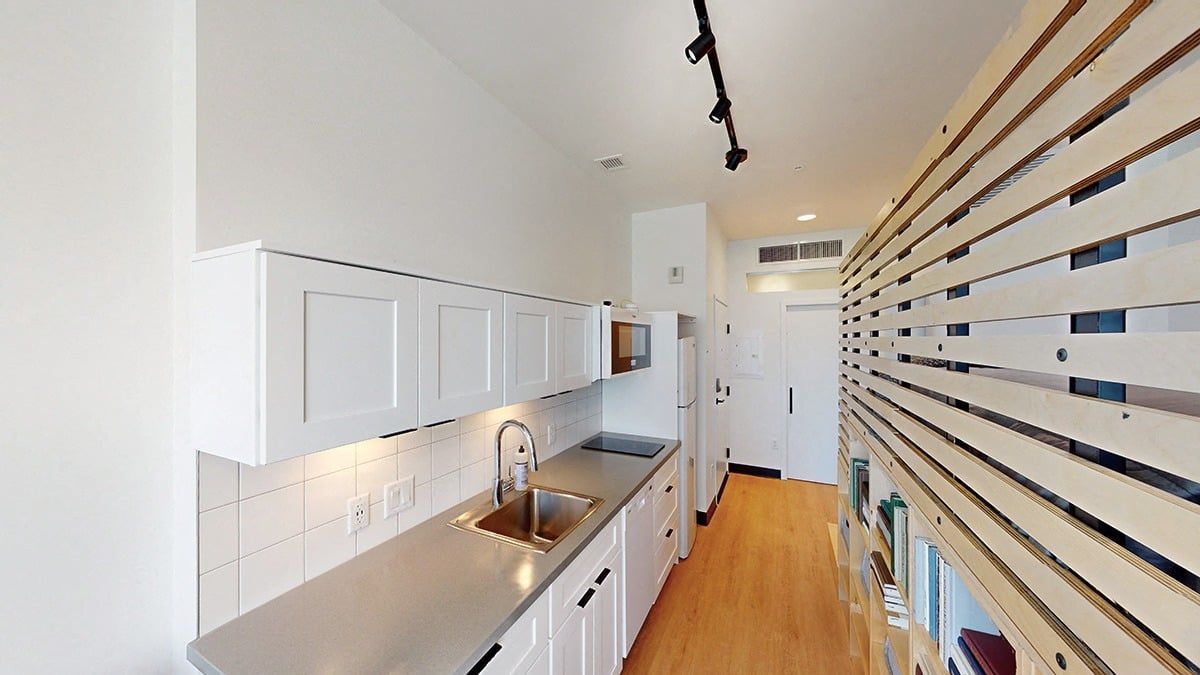 Long, narrow kitchen with white cabinets, silver countertop, and wooden accent wall.