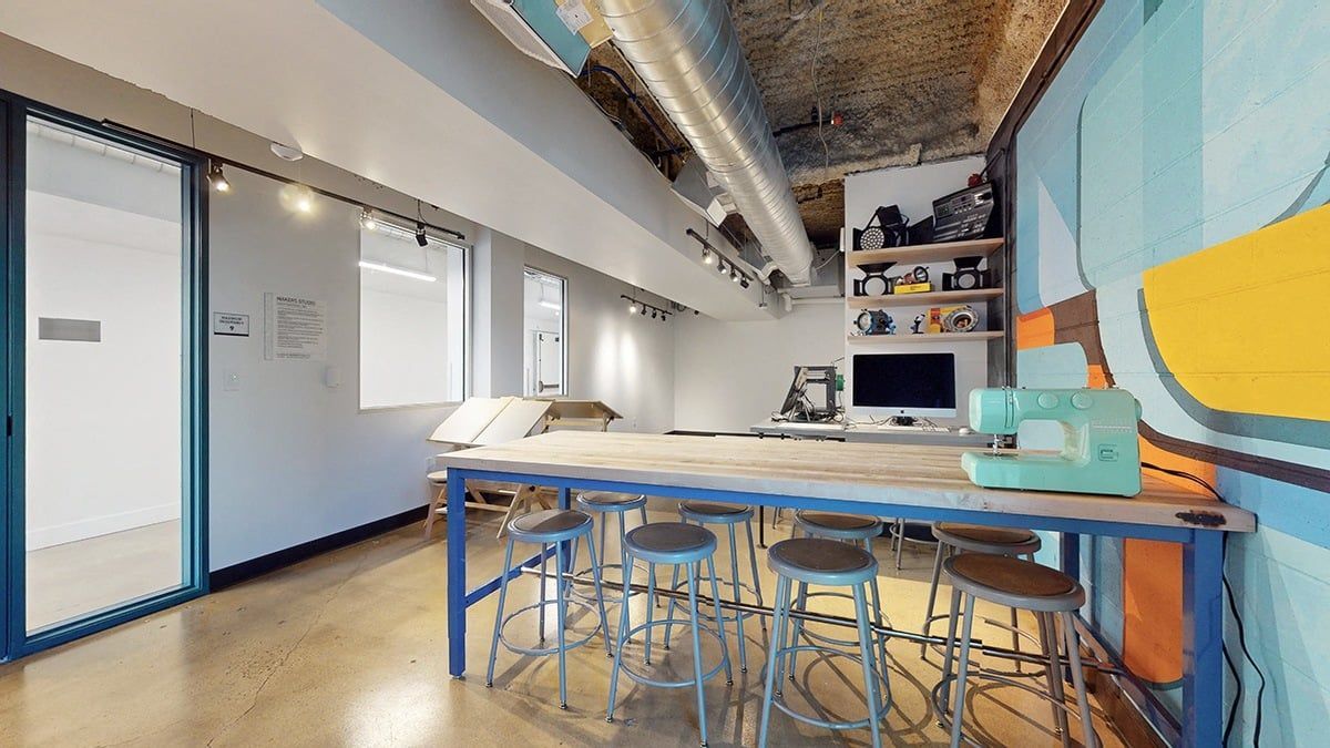 Art studio with a long table, stools, sewing machine, and colorful mural.