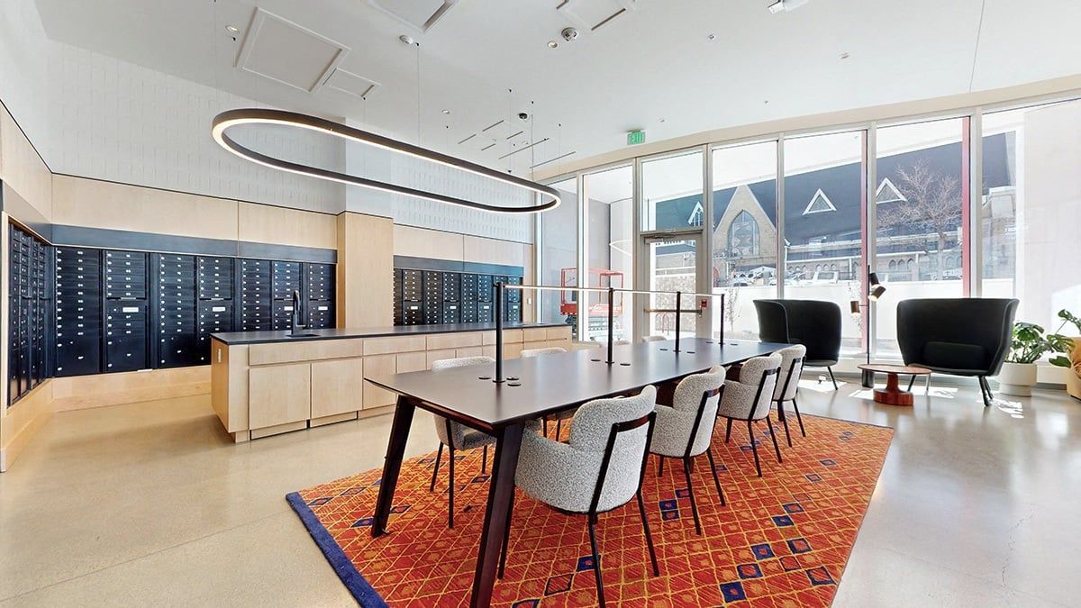 Modern co-working space with a long table, chairs, and orange rug. Mailboxes line the wall.