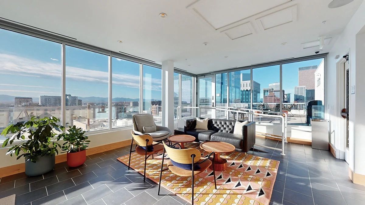 Bright lounge with large windows, city views, modern furniture, and potted plants.