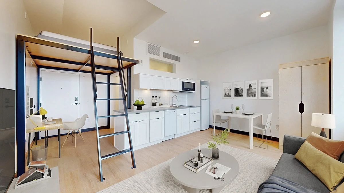 Loft apartment interior with a ladder leading to a sleeping area, kitchen, dining table, and living area.